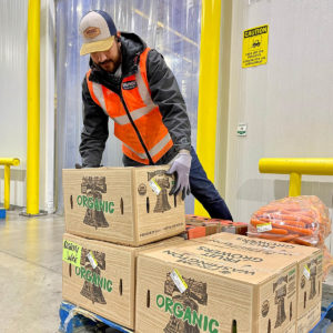 Employee stacking produce on pallet in warehouse.